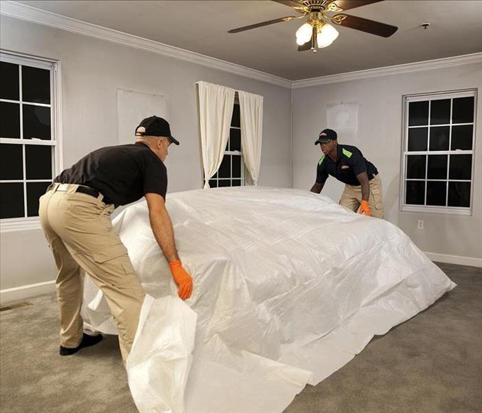 Two SERVPRO team members laying a protective cloth over a couch.